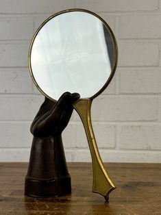 a hand holding a magnifying glass on top of a wooden table next to a brick wall