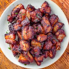 a white bowl filled with cooked meat on top of a wooden table