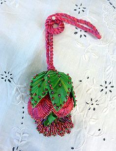 a pink and green beaded ornament on a white tablecloth with lace