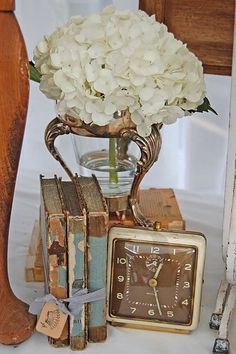 a vase with white flowers sitting on top of an old book next to a clock