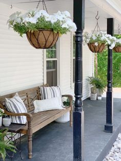 a porch with two hanging planters and a wooden bench on the front porch area