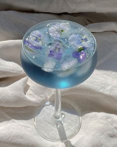 a glass filled with blue liquid and purple flowers