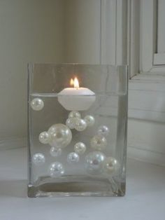 a glass vase filled with white flowers on top of a table next to a window