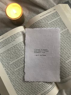 an open book sitting on top of a bed next to a lit candle and paper