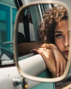 a woman with curly hair sitting in a car looking at herself in the side mirror