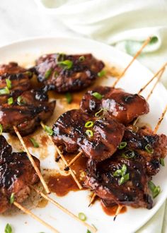 meat skewers with sauce and green onions are on a white plate, ready to be eaten