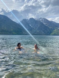 two women are swimming in the water near mountains