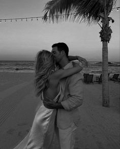 a man and woman kissing under a palm tree on the beach in front of the ocean