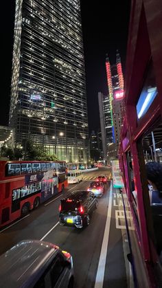 cars and buses are driving down the street in front of tall buildings at night time