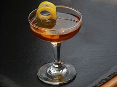 a glass filled with liquid sitting on top of a black table next to a slice of lemon