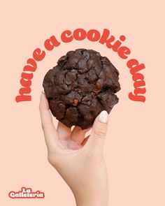 a hand holding up a chocolate cookie with the words have a cookie day on it