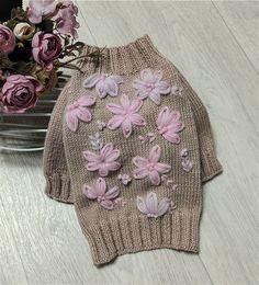 a knitted sweater with pink flowers on it next to a bowl of flowers and a vase