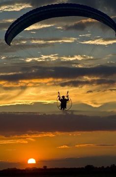 a person is parasailing in the sky at sunset