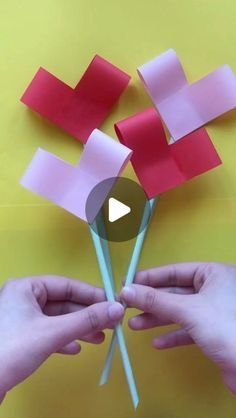 two hands holding red and pink paper flowers with one hand over the other's fingers