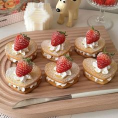 a wooden tray topped with cookies covered in whipped cream and strawberries next to a dog figurine