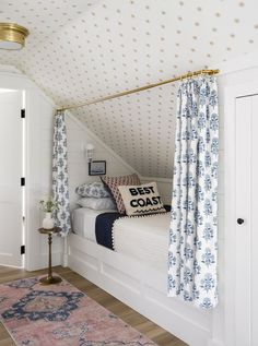 a white bed sitting under a window next to a blue and white rug on top of a hard wood floor