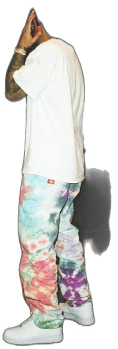 a man in white shirt and tie dye pants standing with his hand on his head