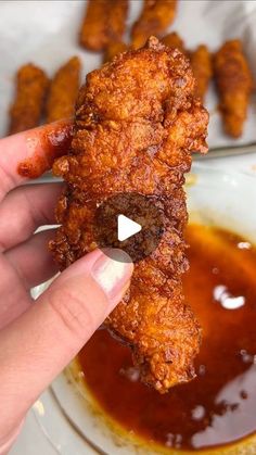 a person is holding up a fried chicken nugget with sauce on the side