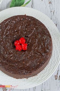 a chocolate cake topped with two cherries on top of a white plate next to a green leaf