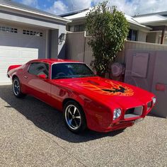 a red firebird car parked in front of a house with two garage doors open