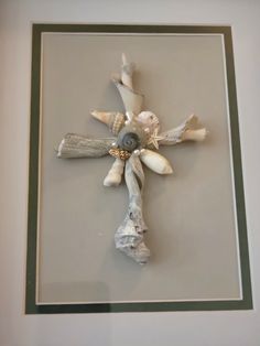 a cross made out of driftwood and seashells is displayed in a frame