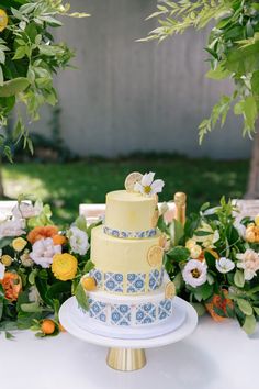 a yellow and blue wedding cake sitting on top of a table next to greenery