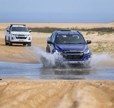 two cars are driving through the water in front of each other on a sandy beach