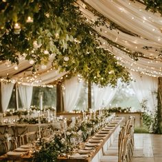 an outdoor tent with tables and chairs covered in greenery, lights and hanging candles