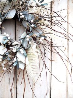 a wreath is hanging on the side of a wooden door with white flowers and green leaves