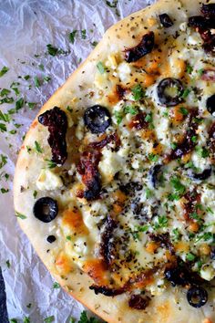 an uncooked pizza with olives, cheese and parsley on paper wrapper