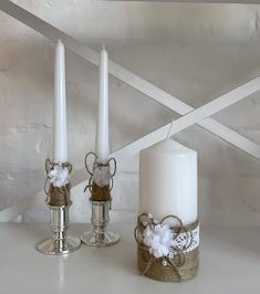 two white candles are sitting next to each other on a table in front of a wall