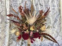 a vase filled with flowers and feathers on top of a lace tablecloth covered surface