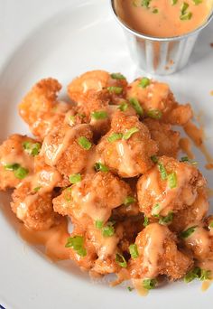 a white plate topped with tater tots next to a cup of dipping sauce