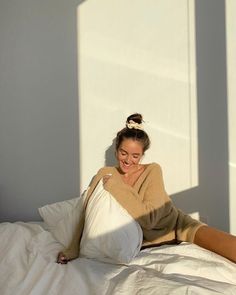 a woman laying on top of a white bed next to a pillow and smiling at the camera