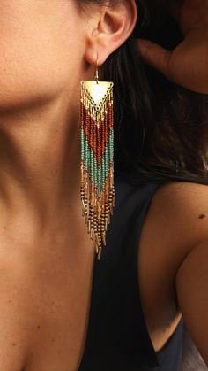 a close up of a woman's ear wearing gold and green beaded earrings