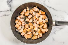 chicken and carrots cooking in a skillet on a marble counter top