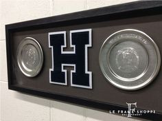 two silver and black trophies are displayed in a shadow box with the letter h on it