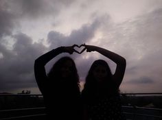 two girls making a heart shape with their hands in front of the sky and clouds