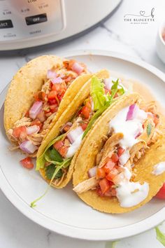 two chicken tacos on a plate next to an instant pot