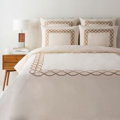 a bed with white linens and brown trim on the comforter in a bedroom