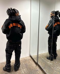 a person standing in front of a mirror wearing a black jacket with orange writing on it