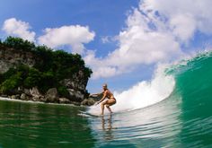 a woman riding a surfboard on top of a wave in the ocean next to a small island