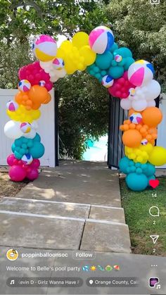 an arch made out of balloons on the side of a sidewalk in front of a white fence