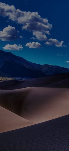 the sky is full of clouds over sand dunes and mountains in the distance are seen