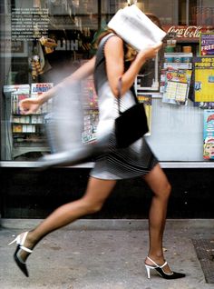 a woman is running down the sidewalk in front of a store with her handbag