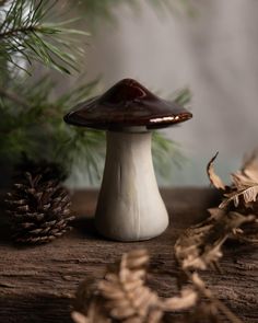 a small mushroom sitting on top of a wooden table next to pine cones and leaves