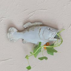 a fish statue hanging from the side of a wall with green leaves on it's head