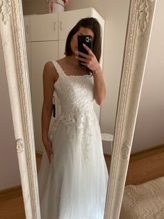 a woman taking a selfie in front of a mirror wearing a white wedding dress