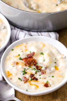 two white bowls filled with potato soup on top of a wooden table next to a silver pot