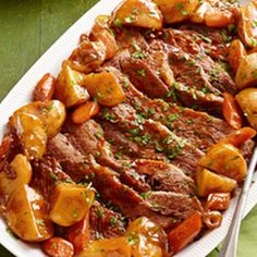 a white plate topped with meat and potatoes on top of a green table next to a fork